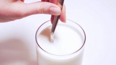 Kadın eli, çiftlik yoğurdunu kaşıkla dairesel hareketlerle karıştırır. Beyaz arka planda şeffaf bir bardakta taze soya sütü.