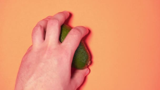 Avocado 's delen op perzikkleurige achtergrond, close-up. Avocado 's in een vrouwen- en herenhand, een bovenaanzicht — Stockvideo