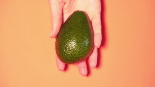 Aguacate hermoso y maduro en una mano de las mujeres primer plano sobre un fondo de color, aislado — Vídeos de Stock