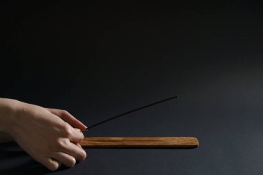 Bir kadın, siyah arka plandaki ahşap bir standa aromatik bir sopa yerleştirir.