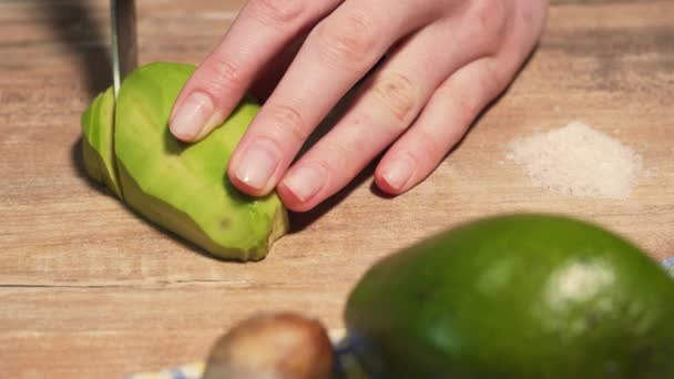 Weibliche Hände schneiden reife Avocado mit einem Küchenmesser in Scheiben. Guacomole in Nahaufnahme auf Holztisch kochen — Stockvideo