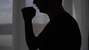 Pencere arkasında öksüren bir adamın silüeti. Hasta Covid-19 virüsü için evinde tedavi görüyor.