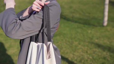 İş kadını omzuna bej bir pamuk torba koyar, yakın plan. Plastiksiz hayat kavramı, tek kullanımlık paketler olmadan mağazaya gitmek