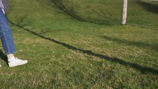 Una mujer en jeans sostiene una bolsa de algodón beige en sus manos y camina por el parque en el césped. Bolsa ecológica natural hecha de materiales reciclados — Vídeos de Stock