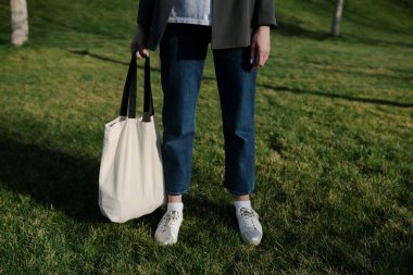 Parktaki yeşil çimlerin arka planında, kadınların elinde beyaz bir çevre torbası. Çevreyi plastikten korumak