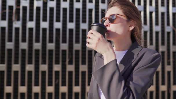 La joven empresaria está desayunando en el parque. Chica en gafas de sol bebe café de soja de vasos de papel reciclado — Vídeos de Stock