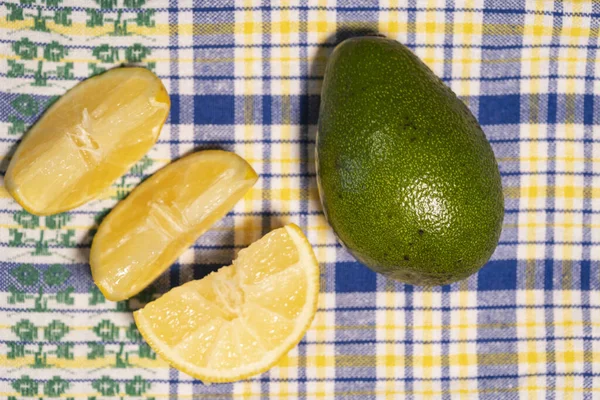 Fresh ripe avocado and sliced lemon wedges lie on a beautiful tablecloth, top view — Stock Photo, Image