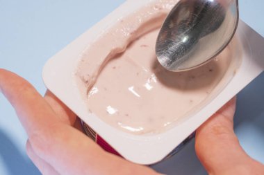 Kaşıkla glütensiz yoğurt yiyen bir kadın. Kadın eli, mavi bir arka planda izole edilmiş kaşık ile süzme bir peynir alır.