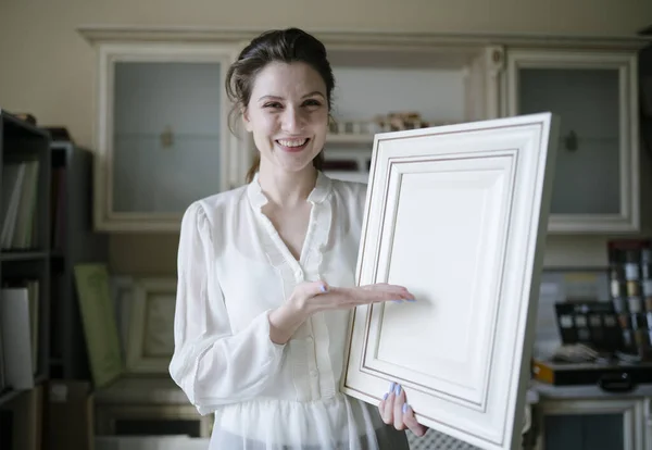 Egy női eladó bemutatja egy példa a bútorok a konyhában. Egy fiatal kisvállalkozó belenéz a kamerába és mosolyog egy bútorboltban. — Stock Fotó