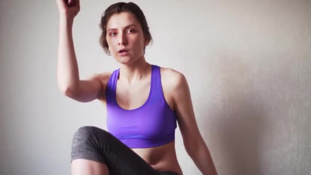 Een mooie vrouw in sportkleding traint thuis, in de slaapkamer. blank meisje horloges online oefening, tijdens zelf-isolatie — Stockvideo