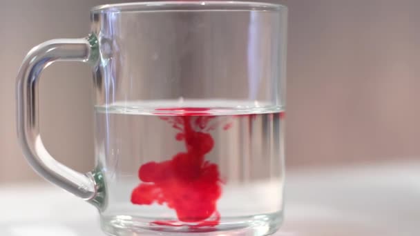 Colorante alimentare rosso viene aggiunto all'acqua in una tazza trasparente. Cucina casalinga — Video Stock