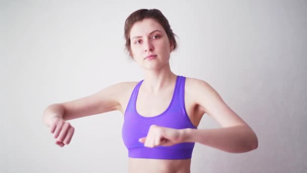 Młoda kobieta w sportowej bluzce uprawia sport w domu. Sportowiec patrzący w kamerę podczas treningu rąk. — Wideo stockowe