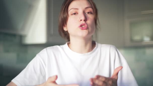 Μια νεαρή γυναίκα μπλόγκερ μιλάει και κοιτάζει στην κάμερα, στο βάθος της κουζίνας. Το κορίτσι καταγράφει το βίντεο-μπλογκ με μια ειδική εφαρμογή. Video call, βίντεο εκμάθησης — Αρχείο Βίντεο