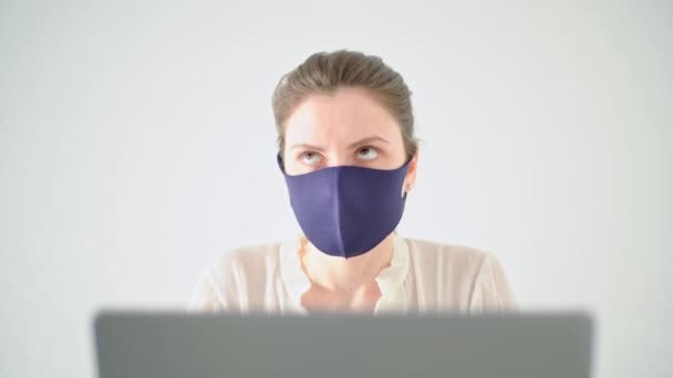 Avsluta karantänen. Ung kvinna arbetar på ett kontor på en bärbar dator, trött på karantänåtgärder, irriterad, tar av en medicinsk mask på en vit bakgrund — Stockvideo