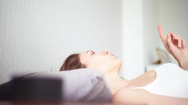 Genç, neşeli bir kadın, akıllı bir asistanın dinamiklerinden müzik dinler ve yatakta dans eder.