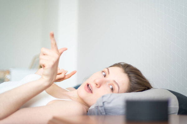 Smart home plays fan music through a portable speaker. Young woman in bed is dancing against the background of a smart speaker