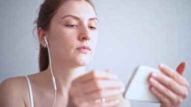 Çevrimiçi film yayını. Kız kulaklığını bir cep telefonuna bağlıyor ve videoyu açıyor.