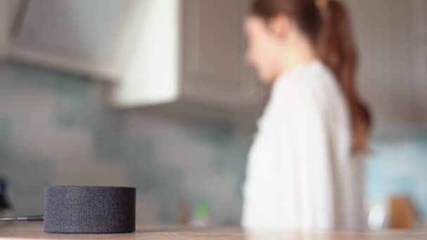 The voice assistant in the kitchen plays music, cheerful girl dances in the background — Stock Video