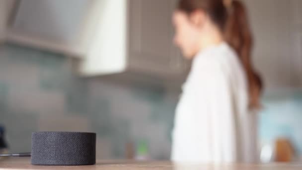 La asistente de voz en la cocina toca música, la chica alegre baila en el fondo — Vídeo de stock