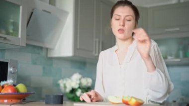 Genç bir kadın dinamik bir şekilde dans ediyor ve bir ses asistanından çalan müzikle birlikte şarkı söylüyor. Akıllı mutfak teknolojisi eğlence getirir.