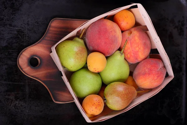 Birnen, Pfirsiche und Aprikosen in einem Korb vor dunklem Hintergrund — Stockfoto