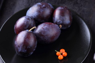 Mavi Erik ve turuncu üvez meyveleri tasarımcı için siyah bir plaka üzerinde