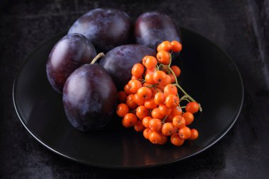 Mavi Erik ve turuncu üvez meyveleri tasarımcı için siyah bir plaka üzerinde