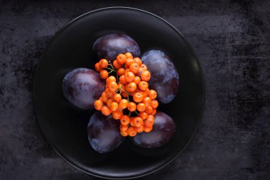 Mavi Erik ve turuncu üvez meyveleri tasarımcı için siyah bir plaka üzerinde