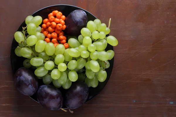 Yeşil üzüm, mavi Erik ve turuncu üvez meyveleri retro tarzı tasarımcısında için siyah bir plaka üzerinde — Stok fotoğraf