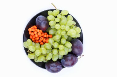 Yeşil üzüm, rowan ve minimalizm tarzı siyah bir plaka üzerinde beyaz bir arka plan üzerinde büyük Erik