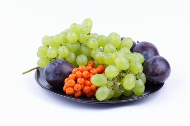 Yeşil üzüm, rowan ve minimalizm tarzı siyah bir plaka üzerinde beyaz bir arka plan üzerinde büyük Erik