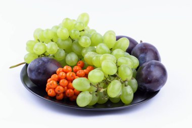 Yeşil üzüm, rowan ve minimalizm tarzı siyah bir plaka üzerinde beyaz bir arka plan üzerinde büyük Erik