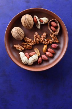 Ceviz ve mavi bir arka plan üzerinde kahverengi kil tabakta fıstık