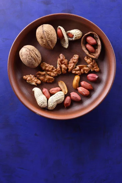 Ceviz ve mavi bir arka plan üzerinde kahverengi kil tabakta fıstık