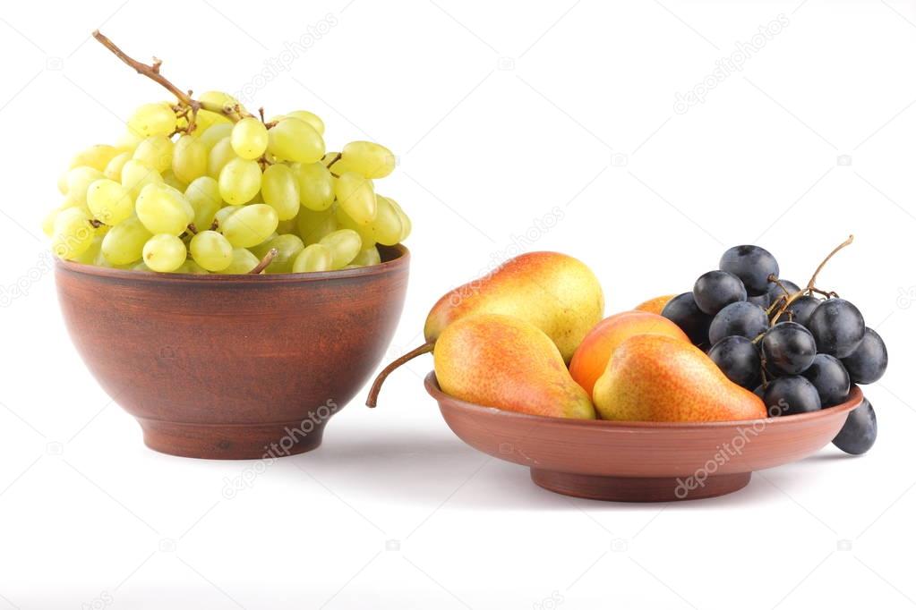 Yellow pears, green and blue grapes in a clay plate on a white background
