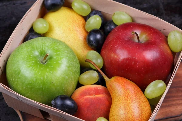 Mela rossa, uva blu scuro, mela verde, pera gialla, uva verde, pesca arancione in una scatola di legno su uno sfondo metallico in stile retrò — Foto Stock