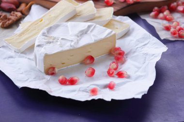 Camembert peyniri, mermer peynir, farklı peynirler, koyu mavi üzüm, kırmızı nar, Yeşil üzüm, fıstık ve ceviz retro tarzı yazmak için boş bir yer ile ahşap bir gemide