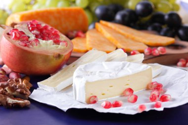 Camembert peyniri, mermer peynir, farklı peynirler, koyu mavi üzüm, kırmızı nar, Yeşil üzüm, fıstık ve ceviz retro tarzı yazmak için boş bir yer ile ahşap bir gemide