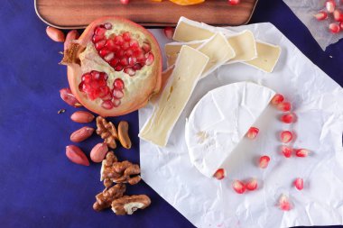 Camembert peyniri, mermer peynir, farklı peynirler, koyu mavi üzüm, kırmızı nar, Yeşil üzüm, fıstık ve ceviz retro tarzı yazmak için boş bir yer ile ahşap bir gemide