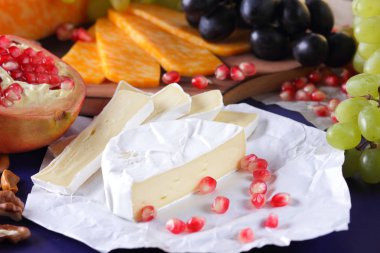 Camembert peyniri, mermer peynir, farklı peynirler, koyu mavi üzüm, kırmızı nar, Yeşil üzüm, fıstık ve ceviz retro tarzı yazmak için boş bir yer ile ahşap bir gemide