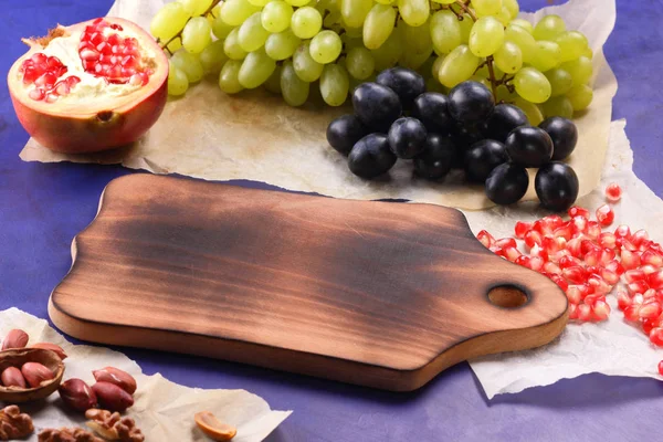 Koyu mavi üzüm, kırmızı nar, Yeşil üzüm, fıstık ve ceviz retro tarzı yazmak için boş bir yer ile ahşap bir gemide