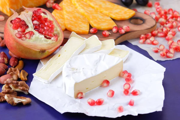 Camembert peyniri, mermer peynir, farklı peynirler, koyu mavi üzüm, kırmızı nar, Yeşil üzüm, fıstık ve ceviz retro tarzı yazmak için boş bir yer ile ahşap bir gemide