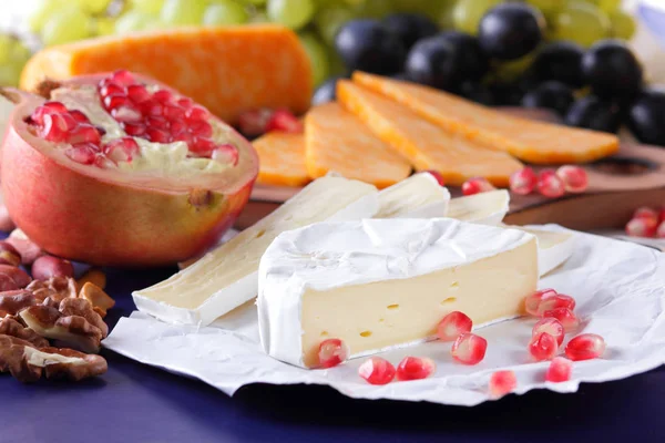 Camembert peyniri, mermer peynir, farklı peynirler, koyu mavi üzüm, kırmızı nar, Yeşil üzüm, fıstık ve ceviz retro tarzı yazmak için boş bir yer ile ahşap bir gemide