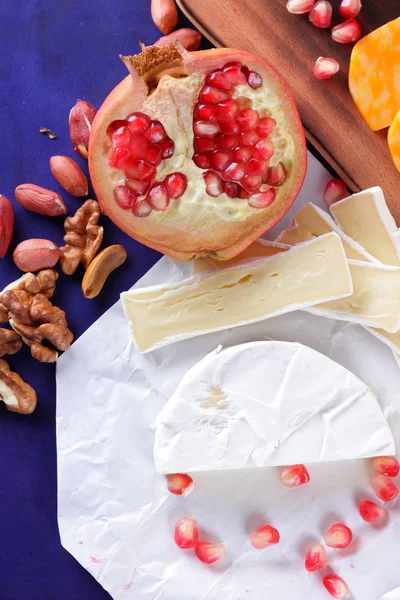 Camembert peyniri, mermer peynir, farklı peynirler, koyu mavi üzüm, kırmızı nar, Yeşil üzüm, fıstık ve ceviz retro tarzı yazmak için boş bir yer ile ahşap bir gemide