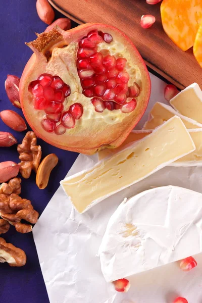 Camembert peyniri, mermer peynir, farklı peynirler, koyu mavi üzüm, kırmızı nar, Yeşil üzüm, fıstık ve ceviz retro tarzı yazmak için boş bir yer ile ahşap bir gemide