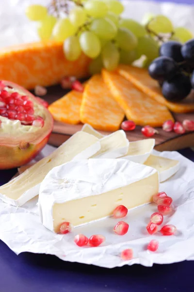 Camembert-Käse, marmorierter Käse, verschiedene Käsesorten, dunkelblaue Trauben, roter Granatapfel, grüne Trauben, Erdnüsse und Walnüsse auf einer Holztafel mit einem leeren Schreibplatz im Retro-Stil — Stockfoto