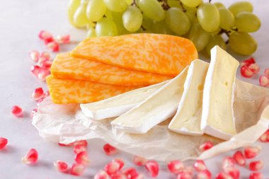 Camembert peyniri, dilimlenmiş peynir, turuncu peynir, peynir bir sürü. Yeşil üzüm ve beyaz zemin üzerine nar taneleri