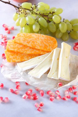 Camembert peyniri, dilimlenmiş peynir, turuncu peynir, peynir bir sürü. Yeşil üzüm ve beyaz zemin üzerine nar taneleri
