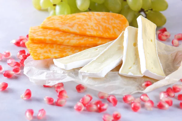 Camembert peyniri, dilimlenmiş peynir, turuncu peynir, peynir bir sürü. Yeşil üzüm ve beyaz zemin üzerine nar taneleri