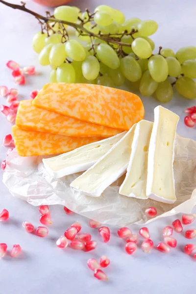 Camembert peyniri, dilimlenmiş peynir, turuncu peynir, peynir bir sürü. Yeşil üzüm ve beyaz zemin üzerine nar taneleri